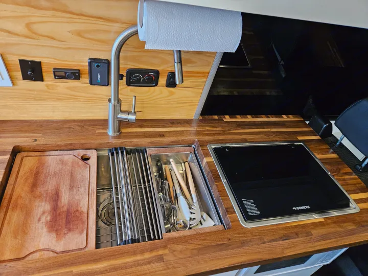 Compact RV rental kitchen features wood countertop, sink, Dometic cooktop, and integrated controls. Ready for adventure!. Mercedes-Benz Sprinter 2021