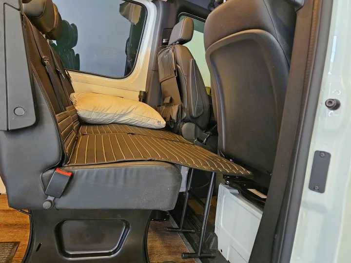 Inside an RV rental, black seats fold down to a flat bed. A cream pillow rests on the padded surface for travel comfort.. Mercedes-Benz Sprinter 2021