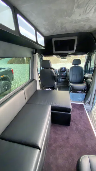 Spacious RV rental van interior featuring black lounge seating that converts to a bed, overhead storage, and front cockpit.. Mercedes-Benz Sprinter 2014