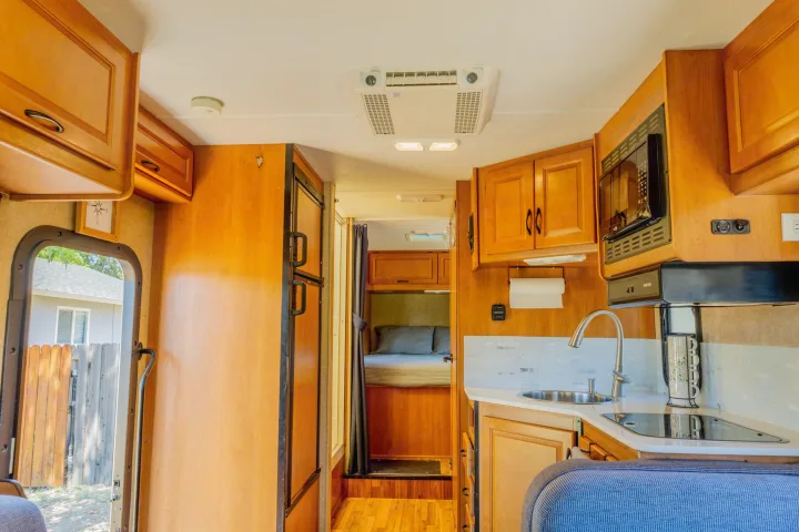 Spacious RV rental interior featuring a kitchen with sink, stove, microwave, and a cozy bedroom area.. Thor Majestic 2015