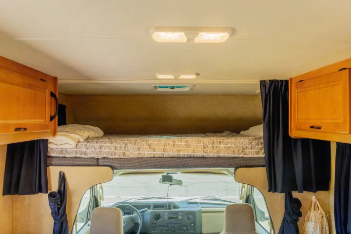 Cozy RV rental interior featuring an overhead bunk bed, front cab, and wooden storage cabinets, ready for adventure.. Thor Majestic 2015