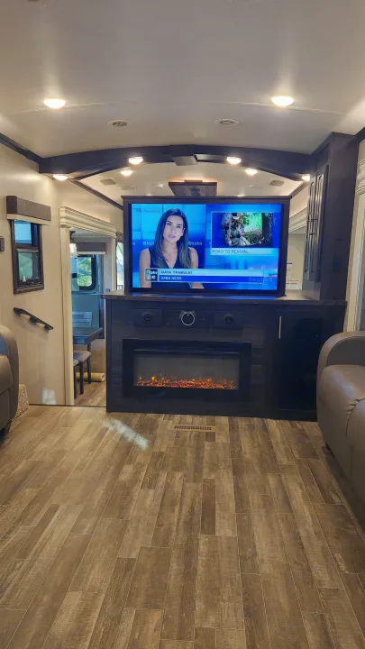 Inside a modern **rv rental**: a comfortable living area featuring a TV, an electric fireplace, and stylish wood-plank flooring.. Jayco North Point 2021