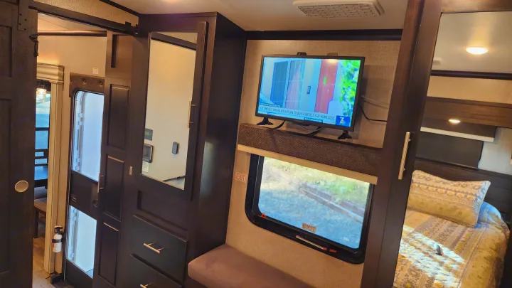 RV rental interior featuring a TV, cozy bedroom, built-in storage with mirror, and window with EXIT sign.. Jayco North Point 2021