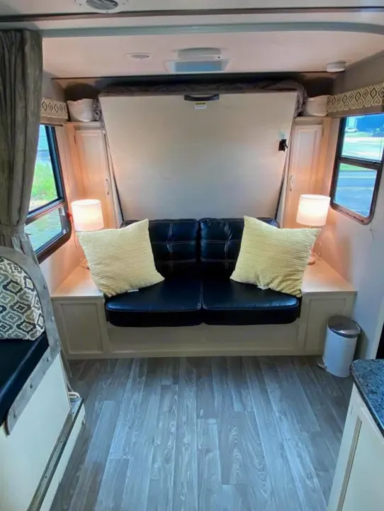 RV rental interior with a black sofa, yellow pillows, lamps, and a space-saving folded Murphy bed.. Winnebago Micro Minnie 2306BHS 2019