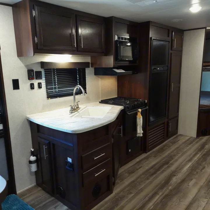 Modern RV kitchen with dark wood cabinets, white counters, sink, stove, microwave, and fridge, perfect for rv rental.. Jayco Jay Flight SLX8 2020