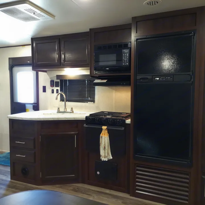 This RV rental interior features a functional kitchen with a large fridge, microwave, stove, and counter with a sink.. Jayco Jay Flight SLX8 2020