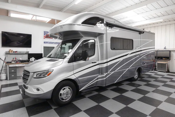 Silver Winnebago motorhome, ideal for rv rental, parked in a well-lit garage with a checkerboard floor.. Winnebago View 2023