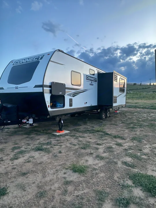 A white 'CONNECT' travel trailer, an RV rental, parked on dirt with its slide-out extended under a cloudy evening sky.. Connect SE 2022
