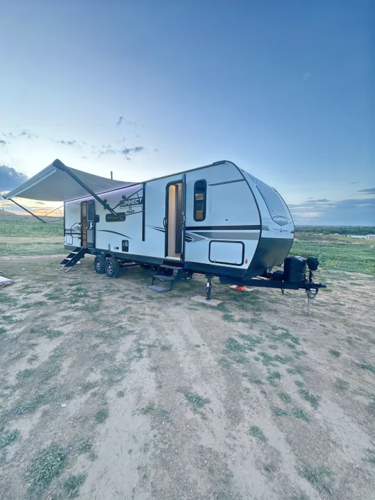 RV rental: A white travel trailer, parked at dusk with its awning extended and lights on, ready for a cozy camping trip.. Connect SE 2022