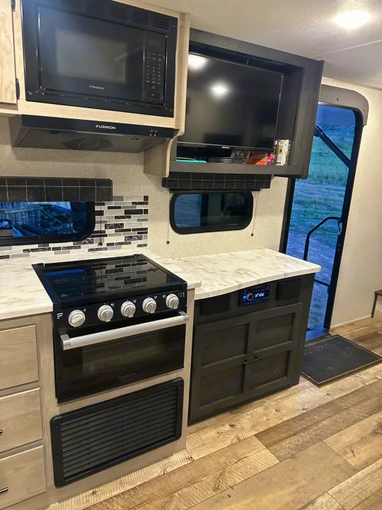 RV rental kitchen: Features Furrion microwave, range, and TV. Light wood cabinets, white counters, and a modern backsplash.. Connect SE 2022