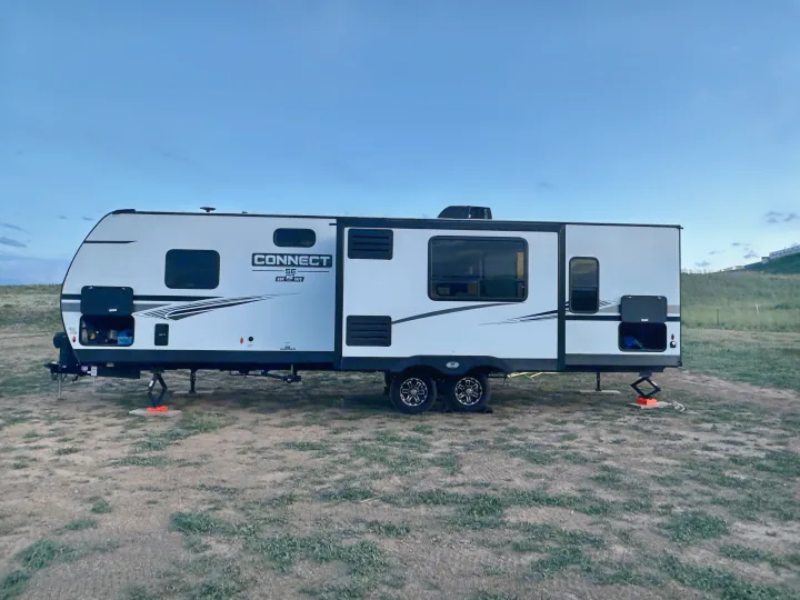 A white KZ Connect travel trailer, possibly an RV rental, is parked for camping, stabilized on dirt ground under a clear sky.. Connect SE 2022