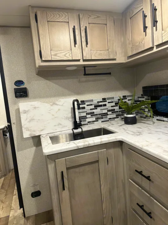 Detailed view of an RV rental kitchen: light wood cabinets, marble counter, modern sink, and mosaic backsplash.. Connect SE 2022