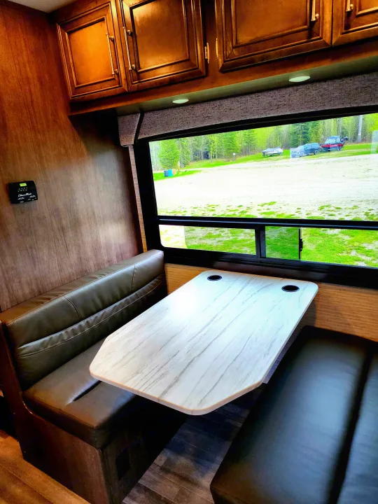 RV rental interior: Cozy dinette with booth seating, wood cabinets, and scenic window view.. Jayco Entegra Odyssey 2024