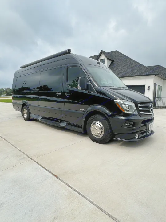 Black Mercedes-Benz Sprinter van, an ideal rv rental, parked on a concrete driveway by a house under cloudy skies.. Midwest Automotive Designs Super Sprinter 2019