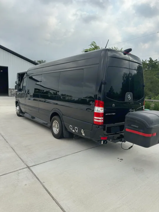 Rear view of a black Mercedes-Benz Sprinter RV rental featuring dual rear wheels and a hitch-mounted storage box.. Midwest Automotive Designs Super Sprinter 2019