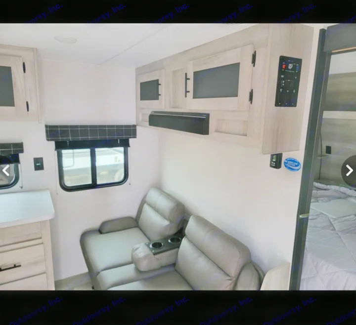 Inside this RV rental: light-toned cabinets, comfortable recliners with cupholders, windows, and a compact bedroom area.. Sportsmen SE 2023