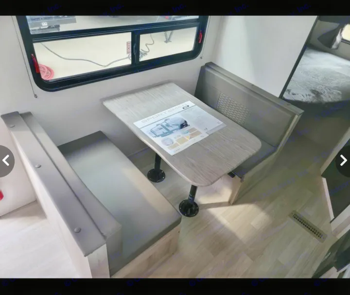 This RV rental interior features a dinette with two cushioned benches and a table, plus a bed visible in the background.. Sportsmen SE 2023