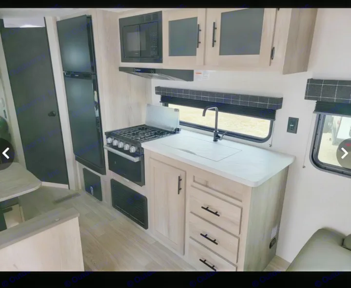 Modern RV rental kitchen inside a camper, featuring stove, microwave, fridge, and sink. Ready for your road trip!. Sportsmen SE 2023