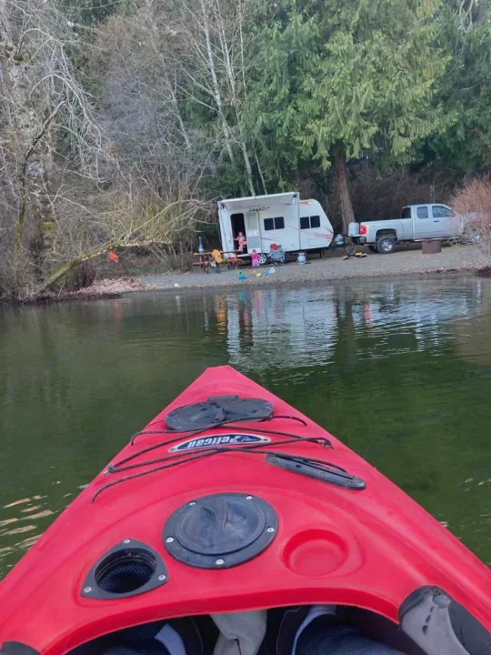 Kayak view of an RV rental setup by the lake, with truck, picnic table, and forest. Lakeside camping.. Takena Takena Trailer 2010