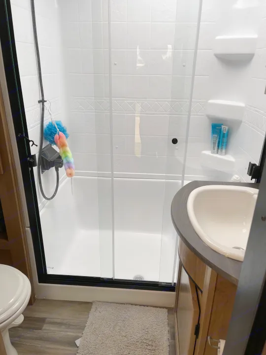 A clean, modern RV rental bathroom. Features a shower with glass doors, a sink, toilet, and bath mat, ready for comfortable travel.. Forest River Sabre 2024