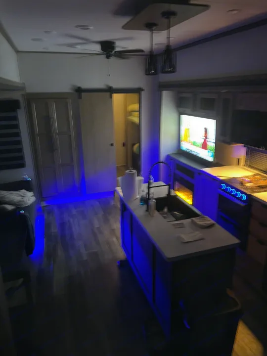 Experience comfort in this RV rental's living and kitchen area, featuring a TV, ceiling fan, and cool blue accent lighting.. Forest River Sabre 2024