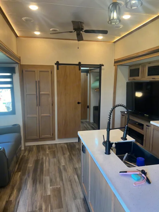 Modern RV rental living space featuring a kitchen island with sink, wood floors, comfy sofa, and barn door.. Forest River Sabre 2024