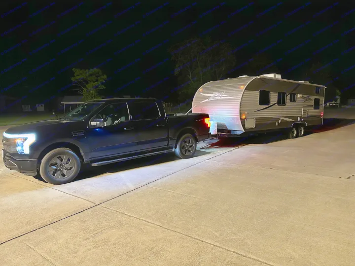 Black Ford F-150 Lightning electric truck towing an RV rental travel trailer at night, headlights illuminating the scene.. Crossroads RV Z-1 2013