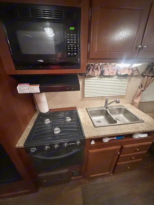 Compact RV rental kitchen featuring a microwave, gas stove, and double sink. Ideal for travel cooking.. Crossroads RV Z-1 2013