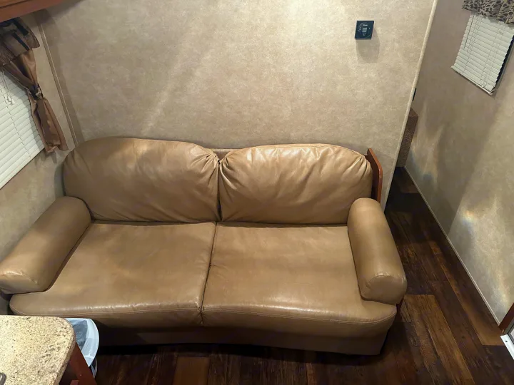 Cozy RV rental interior showing a comfortable tan leather sofa, wood floors, and window blinds.. Crossroads RV Z-1 2013