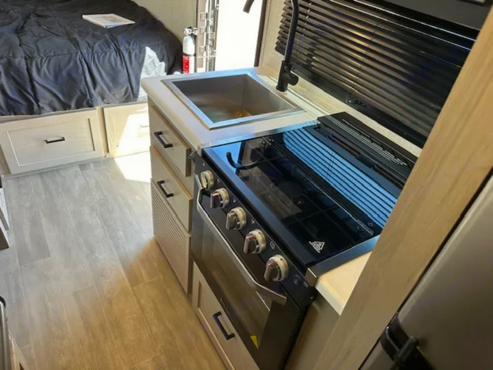 RV rental interior: A compact kitchen area featuring a sink, stove, and oven, adjacent to a bed with storage drawers.. Forest River Flagstaff E-Pro 2023