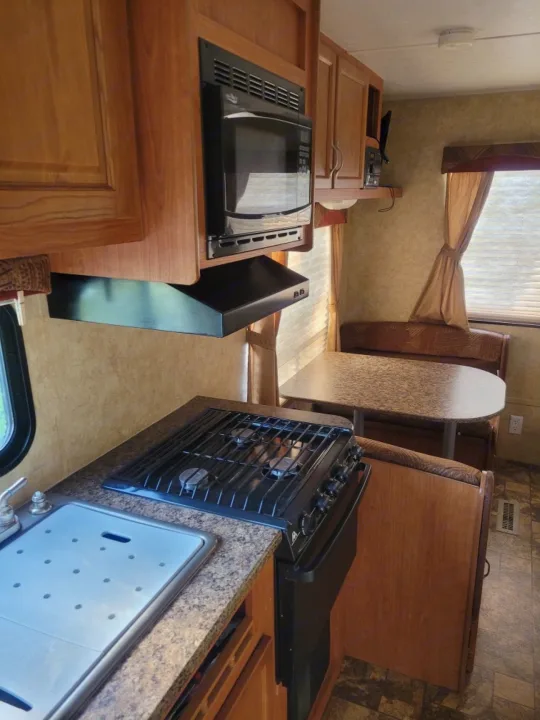 This RV rental interior shows a functional kitchen with microwave, stove, and sink, plus a cozy dinette.. Starcraft Autumn Ridge 2011