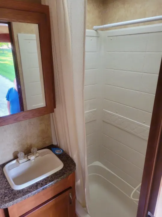 RV rental bathroom showing a vanity with sink and mirror reflecting outdoors, plus a compact white shower stall.. Starcraft Autumn Ridge 2011