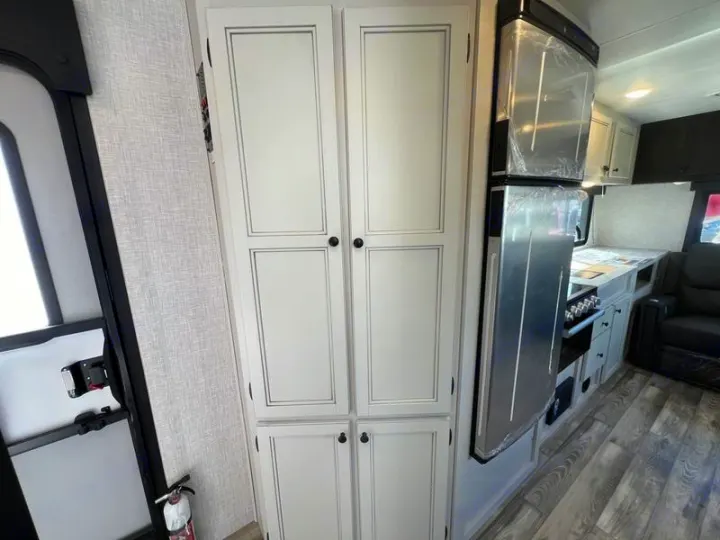 RV rental kitchen area with tall white pantry cabinets, a modern stainless steel refrigerator, and a cooktop.. Open Range Lite 2023