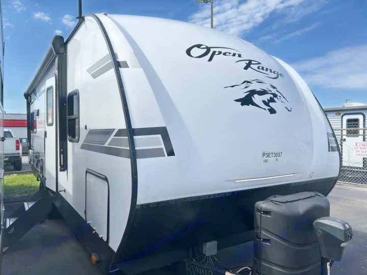 White Open Range RV rental, a travel trailer with propane tanks, parked outdoors on a sunny day.. Open Range Lite 2023