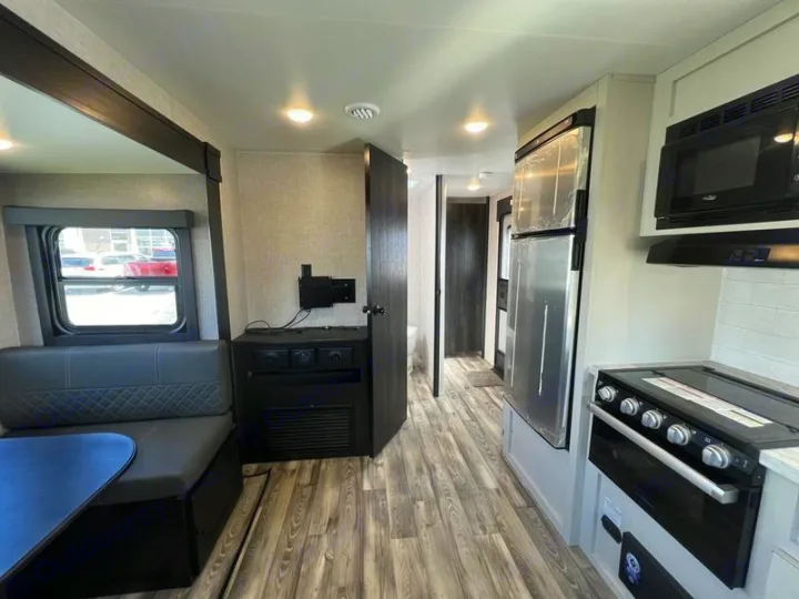 RV rental interior: a modern kitchen with stove, microwave, fridge, and a cozy dinette with window seating.. Open Range Lite 2023