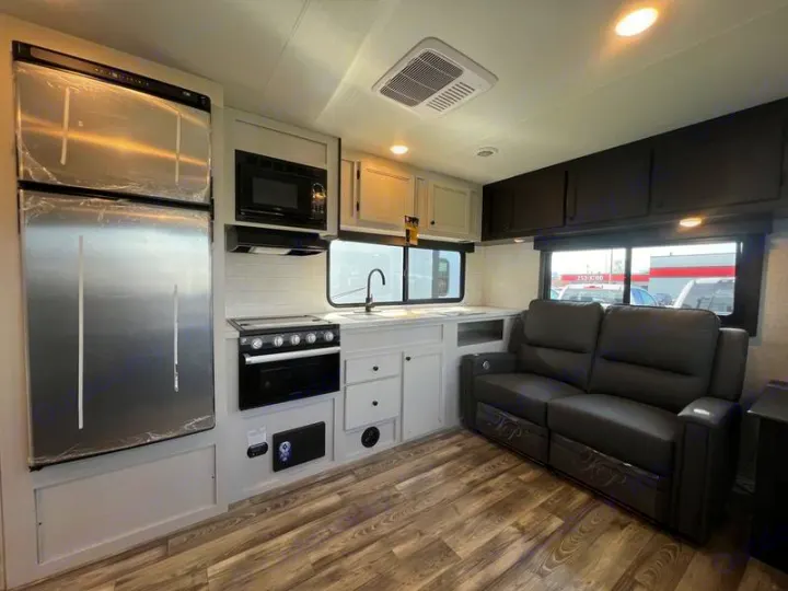 Inside an RV rental: a bright kitchen with a full-size fridge, stove, microwave, and a comfy dark leather sofa by the window.. Open Range Lite 2023