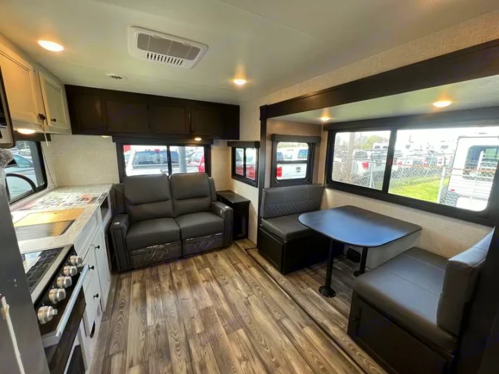 Inside an RV rental: a cozy living area with a kitchen, comfy reclining sofa, and a dinette table with booth seating.. Open Range Lite 2023