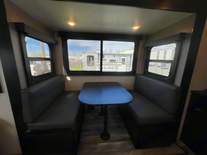 This RV rental dinette features gray upholstered benches, a black table, and large windows for dining or relaxing.. Open Range Lite 2023