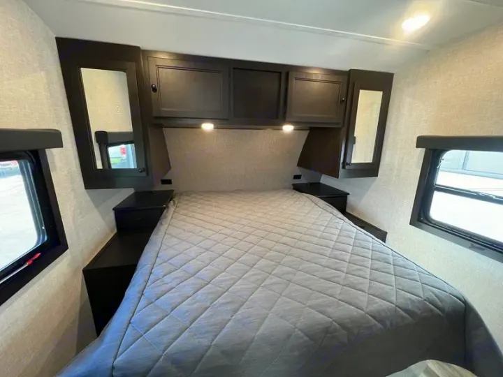 Cozy RV rental bedroom: comfortable bed, dark wood cabinets with mirrors, and windows on both sides.. Open Range Lite 2023