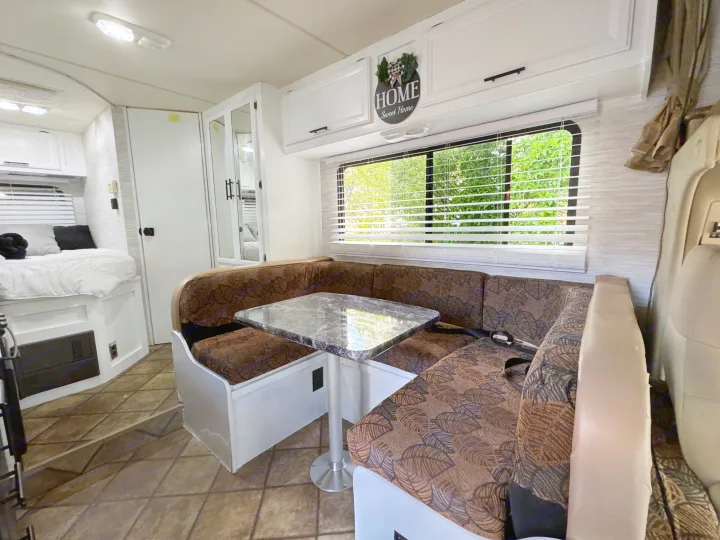 Spacious rv rental interior showcasing a cozy dinette with marble table, leaf-patterned cushions, a bed, and mirrored closet.. Thor Four Winds 2014