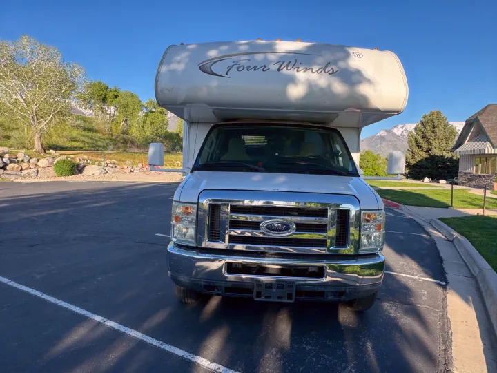 This white Ford Four Winds RV, ideal for rv rental adventures, is parked on asphalt with mountains and trees visible.. Thor Four Winds 2014