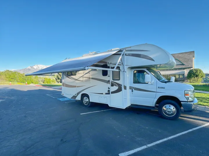 White RV rental with extended awning parked on asphalt, snow-capped mountains in background under clear sky.. Thor Four Winds 2014