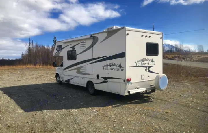A white Yellowstone RV rental is parked on a gravel lot, ready for adventure under a blue sky with clouds and mountains.. Gulf Stream RV 6237 2008