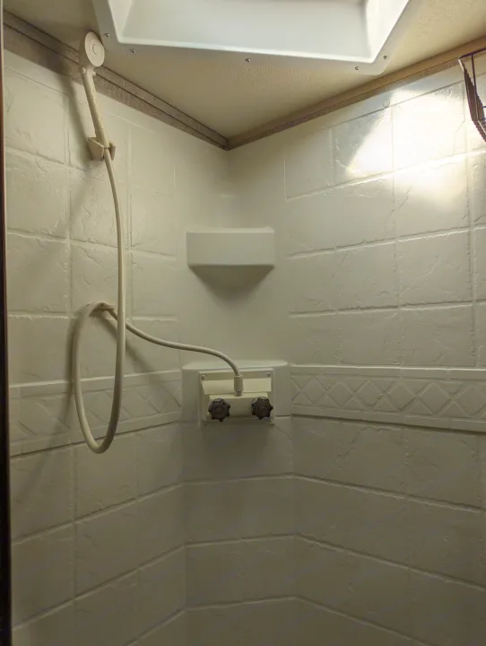 RV rental shower interior featuring textured tiled walls, a handheld showerhead, water controls, and shelf.. Forest River Rockwood Mini Lite 2015