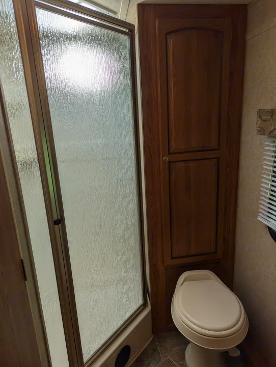 An RV rental bathroom, showing a translucent shower door, toilet, and storage cabinets.. Forest River Rockwood Mini Lite 2015