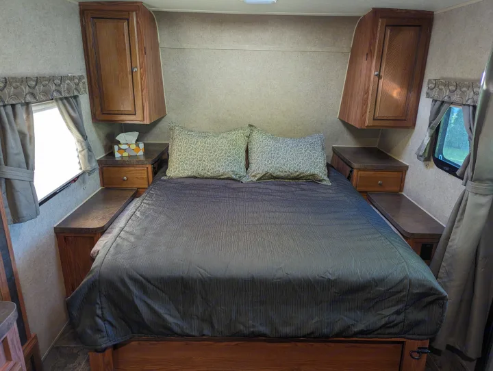 Cozy RV rental bedroom featuring a queen bed, two patterned pillows, wooden cabinets, and windows with curtains.. Forest River Rockwood Mini Lite 2015
