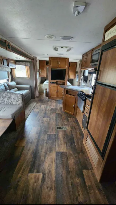 Spacious RV rental interior featuring a full kitchen, living area, and private bedroom with wood-look flooring.. Keystone RV Springdale 2017