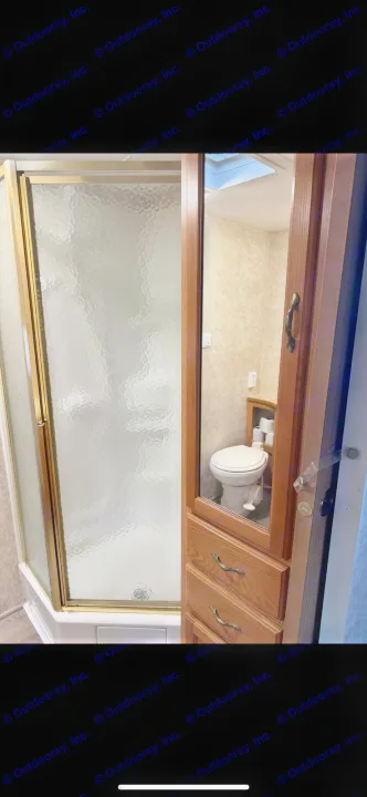 Compact RV rental bathroom featuring a shower stall with textured glass door and a mirrored cabinet reflecting the toilet area.. Keystone RV Cougar 2006
