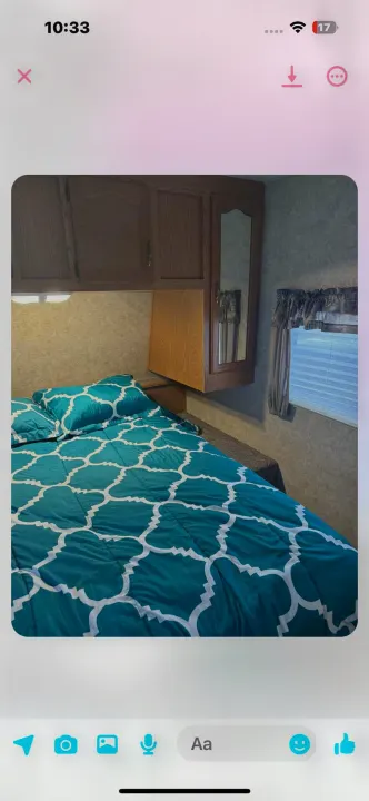 Step inside this RV rental bedroom: a cozy space with teal patterned bedding, overhead wood cabinets, and a window.. Keystone RV Cougar 2006
