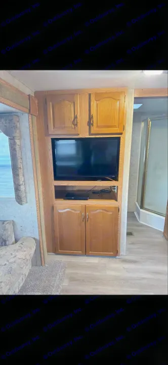 RV rental: Bright interior featuring a wood entertainment center with TV, cabinets, sofa, and a clean shower area.. Keystone RV Cougar 2006
